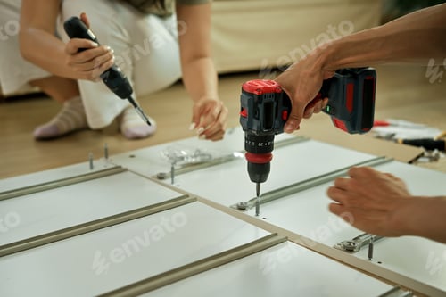 Preview: Closeup couple is working with furniture assembly using electric screwdriver