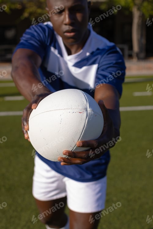 Preview: African American young male athlete holding white rugby ball on field outdoors, focusing on the game