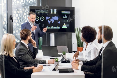 Preview: Serious mature businessman manager stands near big digital wall screen with company financial and
