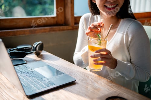 Preview: Freelancer enjoying refreshing orange juice while working on laptop in cafe