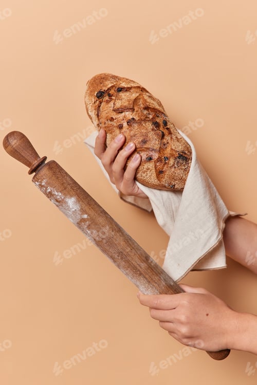 Preview: Unrecognizable person holds homemade crusty appetizing bread wrapped in linen napkin and rolling pin