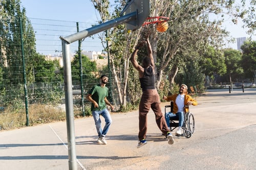 Preview: Young disabled African American man on wheelchair playing basketball sport with friends