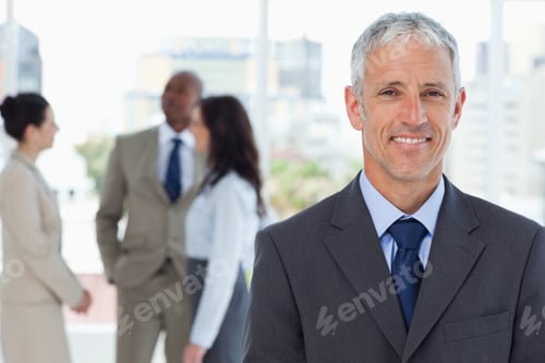 Preview: Mature Smiling Manager Standing Upright In Front Of His Co-Workers