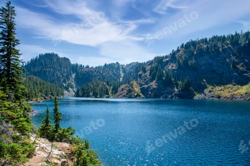 Preview: Dramatic sky over pristine alpine forest blue lake.