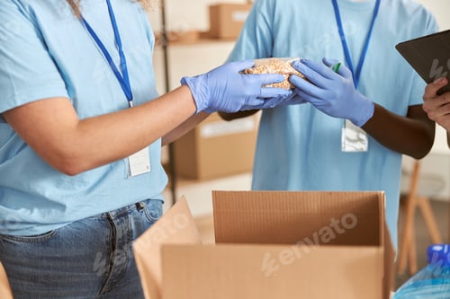 Preview: Close up shot of hands of volunteers in protective gloves sorting, packing food in cardboard