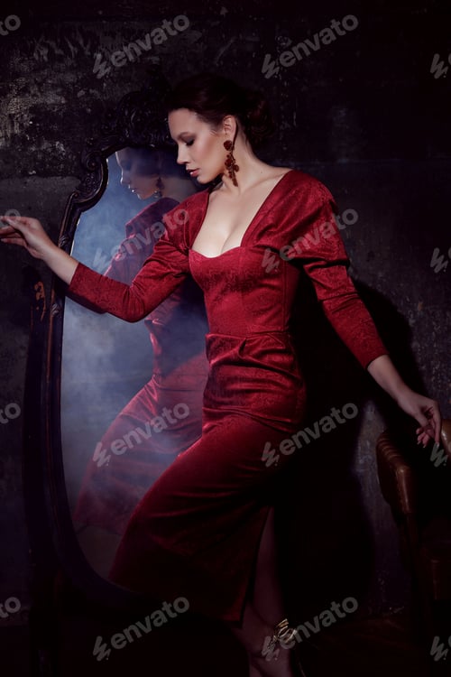 Preview: Beautiful young girl in red dress in retro style in front of mirror, smoke around. Fashion photo