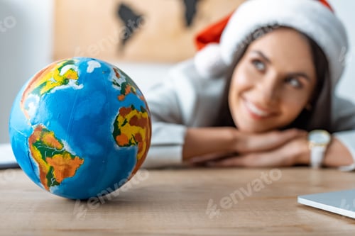 Preview: smiling, dreamy travel agent looking away near globe at workplace