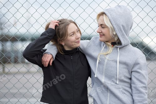 Preview: Two happy female runner friends by wire fence