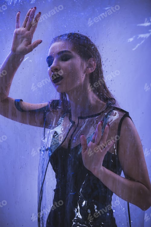 Preview: Fashionable model with wet hair dressed in black swimming suit and transparent rain coat is posing