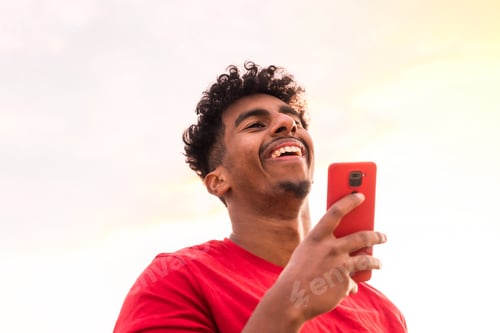 Preview: Arab young man with red t-shirt in a sunset sending a voice note with the mobile in the city