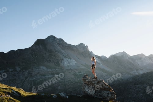 Preview: young girl climbing on a rock at sunset with the landscape of the pyrenees mountains