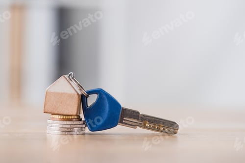 Preview: key with toy house trinket on stack of holden and silver coins on wooden table