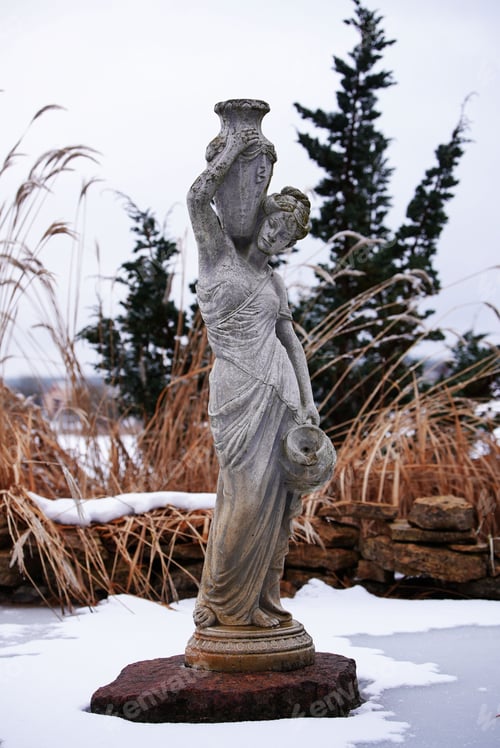 Preview: A statue in the snow, next to grass and bushes.