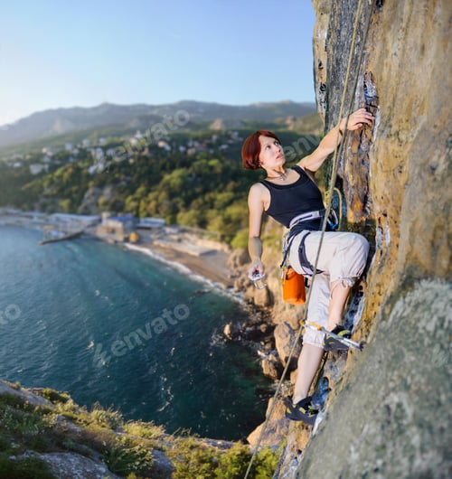Preview: Female climber climbing with rope on a rocky wall
