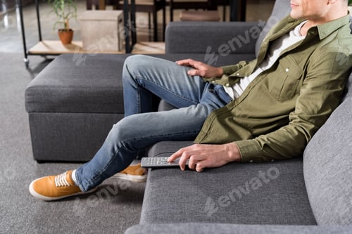 Preview: partial view of man watching tv while resting on sofa at home