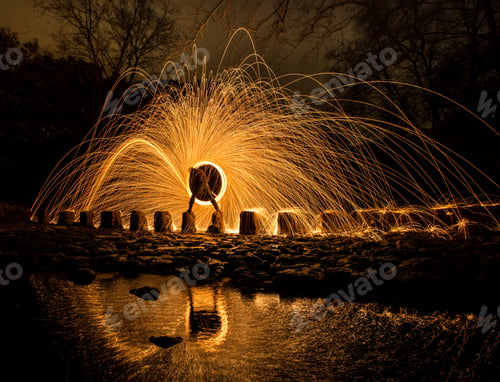 Preview: Person with burning circle on stones between water near hills at night
