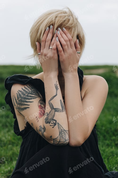 Preview: close-up shot of young woman covering face with hands in front of green field