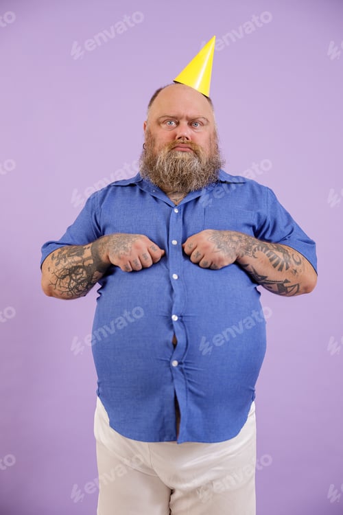 Preview: Displeasured man with overweight in party hat poses on purple background