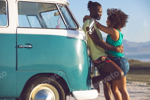 Preview: Side view of romantic mixed race couple embracing each other near camper van at beach