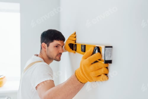 Preview: Handyman in yellow uniform checks levels of wall. House renovation conception