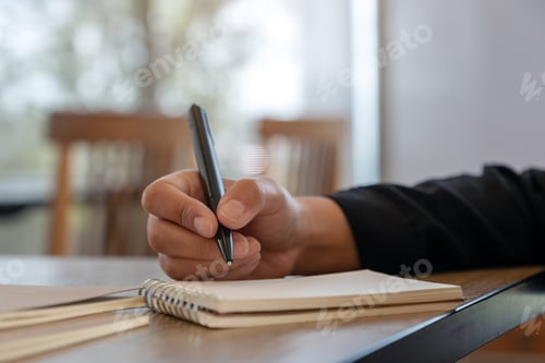 Preview: Closeup image of a hand writing on blank notebook on wooden table