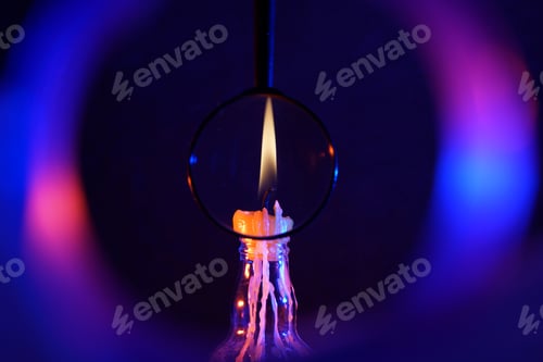 Preview: Closeup of a magnifier against a burning candle on a bottle