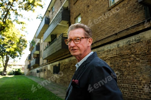 Preview: Senior man wearing glasses and jacket standing near building