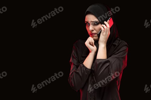 Preview: Portrait of beautiful serious scared frightened young muslim woman wearing black hijab calling for