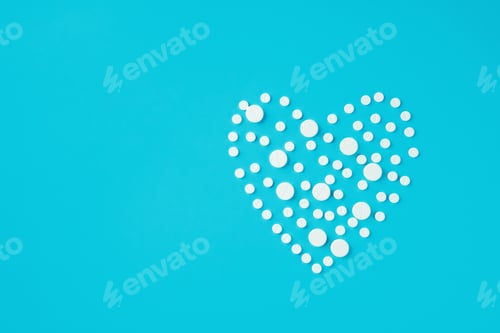 Preview: White round pills of different size in shape of heart on blue background.