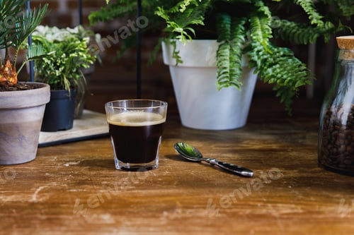 Preview: Morning black coffee in glass on table with plants in coffee shop