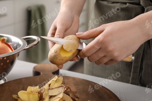 Preview: Woman peeling fresh potato with knife at light table indoors, closeup