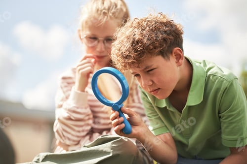 Preview: Caucasian Boy Examining Object with Magnifying Glass While Girl Sitting Nearby