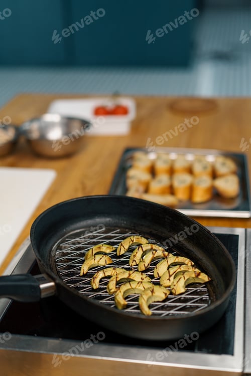 Preview: Professional kitchen chef cooks fresh green avocado in frying pan for frying vegetables