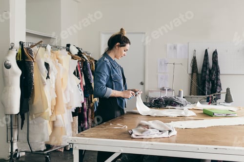 Preview: Young female seamstress cutting pattern in fashion studio