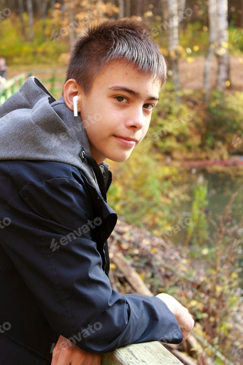 Preview: Beautiful teenager wearing headphones is standing on the bridge leaning on his elbows