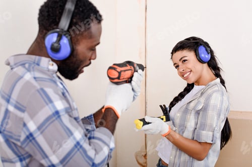 Preview: playful young couple having fun with hammer and drill while making renovation of home