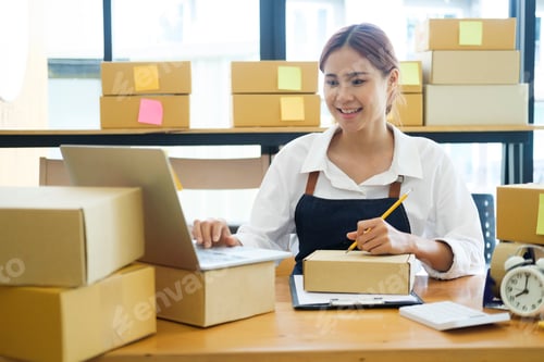 Preview: Asian businesswoman Start up small business owner writing address on cardboard box a.