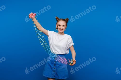 Preview: Beautiful young girl playing with a rainbow slinky, a toy of her childhood on a blue background