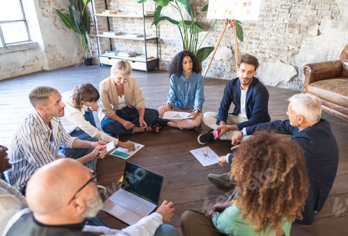 Preview: Multiracial business team is gathered in a circle on the floor, working on a creative project.