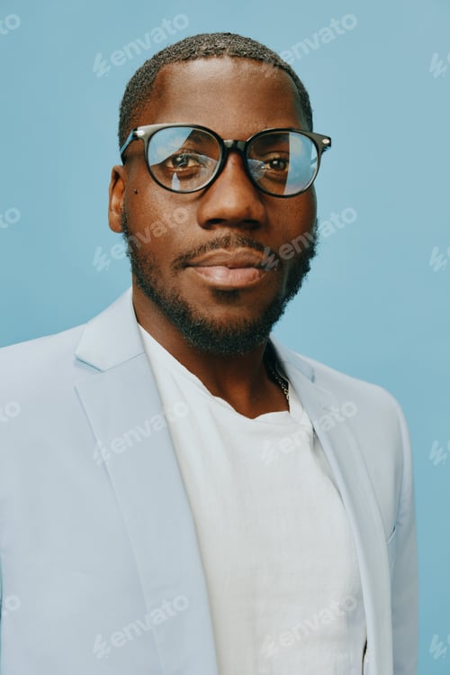 Preview: African man with stylish glasses in a light blue blazer and white shirt, smiling against a soft blue