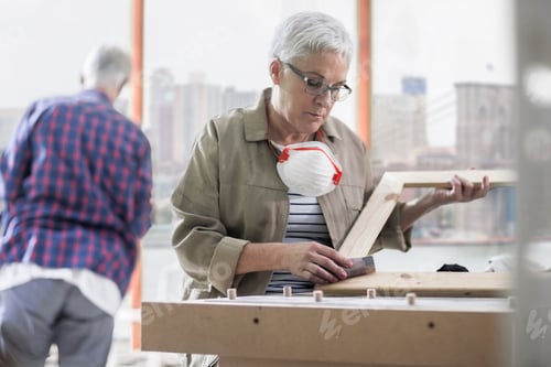 Preview: Mature female carpenter sanding picture frame in furniture making workshop