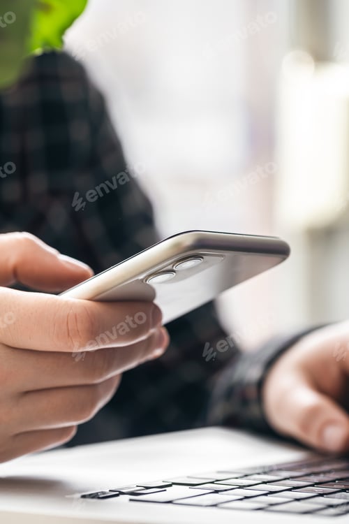 Preview: A man holds a smartphone and works on a laptop.