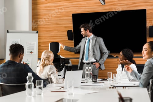 Preview: handsome businessman showing robot to multicultural colleagues sitting in conference hall