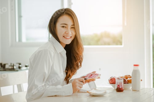 Preview: Smiling Woman Spreads Jam on Bread at Breakfast