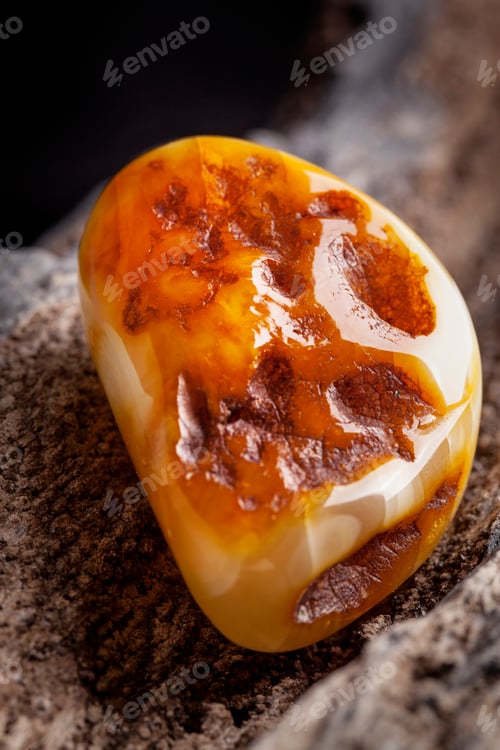 Preview: Natural amber. A piece of yellow opaque natural amber on large piece of dark stoned wood