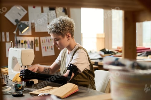 Preview: Young serious female tailor with partial arm concentrating on sewing work