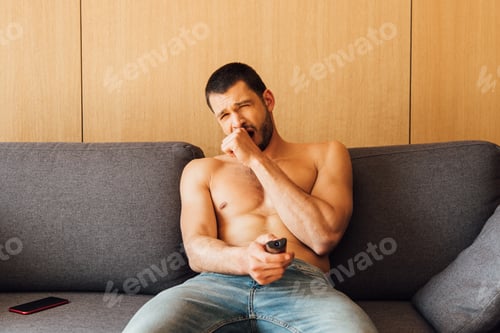 Preview: tired shirtless man in jeans yawning and holding remote controller