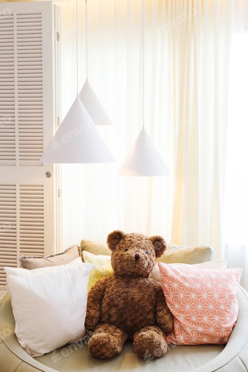 Preview: teddy bear doll sit on sofa with pillow and lamp against curtain and large window in kid bedroom