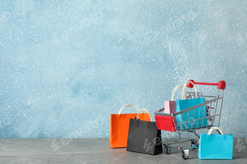 Preview: Small shopping cart and paper bags on grey background, copy space