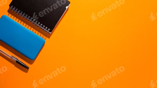 Preview: Top view of a smartphone and a notepad with a pen on an orange background